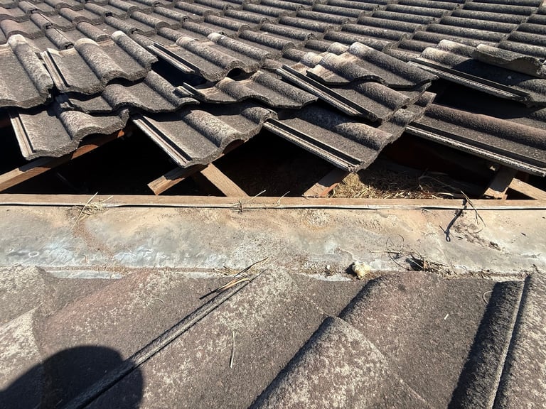 Damaged roof with broken clay tiles exposing wooden framework and gaps, showing deterioration and need for repair