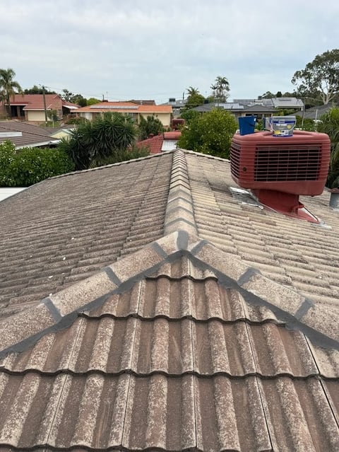 Aerial view of a corrugated metal roof ridge with residential buildings and air conditioning unit in background