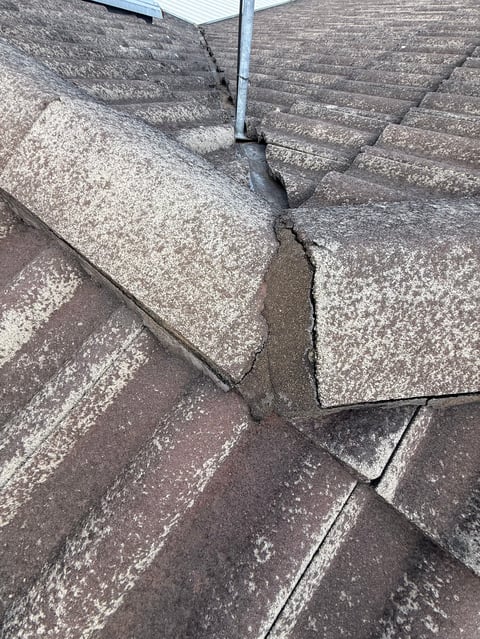 Damaged roof shingles showing separation and wear with visible cracks and displacement along seams